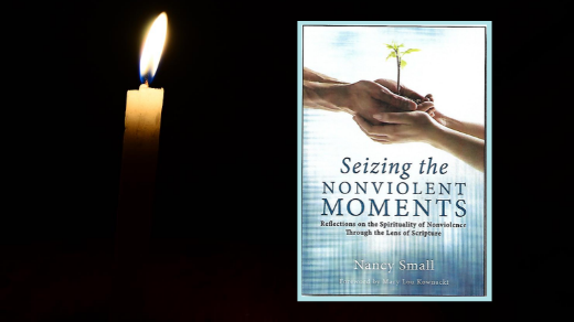 A lit candle illuminates a copy of SEIZING THE NONVIOLENT MOMENT, a book about nonviolence by Nancy Small.